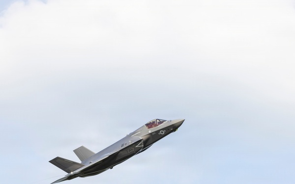 A single military stealth fighter jet is captured in flight against a partly cloudy sky. The aircraft appears to be an F-35 Lightning II, identifiable by its distinctive single-engine stealth design, delta wing configuration, and characteristic fuselage shape. The aircraft is banking slightly, suggesting a maneuver possibly during an airshow or training flight.