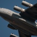 A close-up, low-angle photograph of a U.S. Air Force military transport aircraft in flight against a clear blue sky. The aircraft bears the markings '1102' and '97 AMW' (Air Mobility Wing), identifying it as a C-17 Globemaster III. The image captures the nose, fuselage, and multiple jet engines in sharp detail with dramatic perspective.