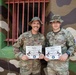 Two U.S. Army soldiers are posing proudly in front of a camouflage-painted wall, each holding a diploma from the Combined Jungle Training Center - South. Both soldiers are wearing OCP (Operational Camouflage Pattern) uniforms with jungle/boonie hats and have earned 'Jungle Expert' certifications from the Jungle Operations Training Course. Their name tapes read 'BONILLA' (left) and 'VALENTIN' (right).