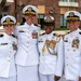 Four U.S. Navy officers in white dress uniforms pose together outdoors, smiling for a group photo. They display various medals, ribbons, and rank insignia consistent with senior officer grades. The setting appears to be near a military or government facility.