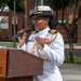 A high-ranking U.S. Navy officer in dress whites is speaking at a podium during an outdoor ceremony. The officer wears a combination cover with gold insignia, shoulder boards indicating senior officer rank (Captain or Admiral), gold aiguillettes, and multiple service ribbons. The podium bears the label 'NRSW' and 'NT PERSONNEL UNIT', suggesting a Naval Reserve or Naval Station Southwest event.