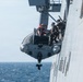 A rigid-hull inflatable boat (RHIB) is being deployed or recovered via davit crane on the side of a large naval vessel at sea. Several personnel in military tactical gear are visible on or near the boat during the operation. The image appears to document a maritime boarding or launch/recovery evolution.