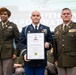 Three military personnel are posing for a formal photograph at what appears to be a Palmetto Military Academy Hall of Fame induction ceremony. The central figure, identified on the certificate as COL Richard J. Zeigler III, is holding a framed Hall of Fame certificate. The event appears to be held in South Carolina, as indicated by the 'South Carolina Army National Guard' banner visible in the background.