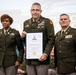 Three military personnel in U.S. Army dress uniforms pose together at what appears to be a formal ceremony. The central figure, identified on the certificate as COL Timothy M. Cassel, is holding a Palmetto Military Academy Hall of Fame induction certificate. The event appears to be taking place at a military academy in Columbia, South Carolina.