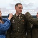 A military promotion ceremony for a South Carolina Army National Guard soldier named Bryngelson, during which new rank insignia are being pinned onto his shoulders. A woman in a blue floral dress pins one shoulder while an older male officer in Army greens pins the other. The event takes place in a formal indoor setting with a projected backdrop displaying the South Carolina Army National Guard emblem.