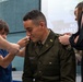 A U.S. Army officer named Suarez is having rank insignia pinned onto his uniform collar during what appears to be a military promotion ceremony. Family members, including a young boy and a woman in a black dress, are participating in the traditional pinning ritual. The ceremony appears to take place in an indoor venue with Army-related signage visible in the background.