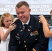A U.S. Army officer named Oelfke, wearing dress blues, is having rank insignia pinned onto his shoulders by two children during what appears to be a promotion ceremony for the South Carolina Army National Guard. The officer is smiling broadly as a young red-haired girl pins his left shoulder and a boy in a blue striped shirt pins his right. The setting is an official military ceremony with a South Carolina Army National Guard banner visible in the background.