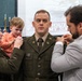 A military promotion ceremony is taking place, likely within the South Carolina Army National Guard based on the projection screen in the background. A soldier named Thomas is having new rank insignia pinned onto his uniform collar by two individuals — a female soldier in Army greens holding a young child, and a civilian man in a plaid blazer. The ceremony appears to be an intimate, formal occasion with family participation.