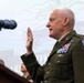 A senior U.S. Army officer in dress green uniform is raising his right hand, appearing to take an oath or be sworn in at a formal proceeding. He stands at a podium with a microphone, wearing numerous service ribbons, badges, and a South Carolina National Guard shoulder patch. Other uniformed personnel are visible in the background.