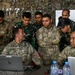 A group of U.S. Army soldiers and what appear to be Indonesian military personnel (TNI-AD) are gathered around laptops in a field operations center covered with camouflage netting. The session appears to be a joint military planning or training exercise, with personnel reviewing information on HP laptops and a whiteboard in the background. Name tapes visible include SANCHEZ, VARGAS, ACASIO, and VELASCO on U.S. Army uniforms.