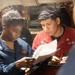 Two U.S. Navy personnel are reviewing a document together in what appears to be a shipboard interior space. The sailor on the left is wearing a blue Navy uniform, while the sailor on the right is wearing a red coverall jacket with 'U.S. NAVY' and a partial name tag reading 'BORIO' visible. They appear to be conducting an inspection or reviewing technical documentation.