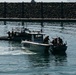 The image shows a maritime law enforcement or military interdiction exercise/operation in a harbor or port area. A marked patrol vessel labeled 'AERONAVAL' is escorting or intercepting a smaller civilian-style boat with individuals aboard raising their hands. A second tactical vessel with armed personnel is visible in the background.