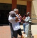 Two individuals are sharing an emotional embrace in front of a building entrance while a group of onlookers applauds around them. The scene appears to be a celebratory or reunion moment, possibly at a government or military facility given the presence of a person in military uniform. The crowd's applause and smiling expressions suggest a positive, significant occasion.