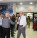A formal reception or farewell ceremony is taking place in the lobby of the U.S. Army Installation Management Command headquarters. Two civilians in the center are shaking hands while a crowd of military personnel in Army Combat Uniforms and civilians line both sides, applauding. The setting suggests an official recognition, welcome, or departure event.