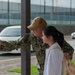 A U.S. Navy service member in digital camouflage uniform is taking a selfie with a young woman near a parking area. The sailor, whose name tape reads 'NARANJILLA,' has their arm around the woman while extending a smartphone outward. The setting appears to be a military installation, likely in Japan based on the vehicle styles and infrastructure.