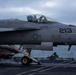 A U.S. Navy carrier-based jet aircraft numbered '213' is captured during a catapult launch from an aircraft carrier flight deck. The aircraft bears visible markings including a pilot name 'LT T.Z. HARITAN' with callsign 'TWINKLE TOES' and a crew chief dedication to 'ADAN ALMONTEOTERO, SAN JUAN, PUERTO RICO'. A flight deck crew member in a green jersey is visible in the background.