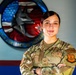 A U.S. Air Force service member poses with arms crossed in front of a unit emblem on a wall. The individual is wearing OCP (Operational Camouflage Pattern) uniform with visible name tape reading 'ELLER' and a Senior Airman rank insignia. The background features a squadron patch identified as a Contracting Squadron emblem incorporating an aircraft and American flag elements.