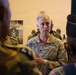 A U.S. Army Colonel named Walliser is engaged in conversation with several foreign military officers in what appears to be an indoor military briefing or meeting environment. He is wearing OCP (Operational Camouflage Pattern) uniform with a Colonel's eagle rank insignia visible on his chest. The setting suggests a multinational military engagement or partnership event.