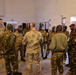 A group of military personnel from multiple nations are gathered in a circle inside an indoor facility, appearing to be engaged in a briefing or discussion. The group includes both Western (likely US) and African military officers wearing various camouflage uniforms and distinctive berets. The setting appears to be a training or conference facility, suggesting a multinational military exercise or cooperation event.