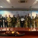 A group of approximately 13 individuals pose for a formal group photograph in front of a Republic of Botswana Ministry of Health branded backdrop. The group includes both military personnel in camouflage uniforms and civilians in business attire. The setting appears to be a conference or meeting room, suggesting an official diplomatic or cooperative health-related engagement.