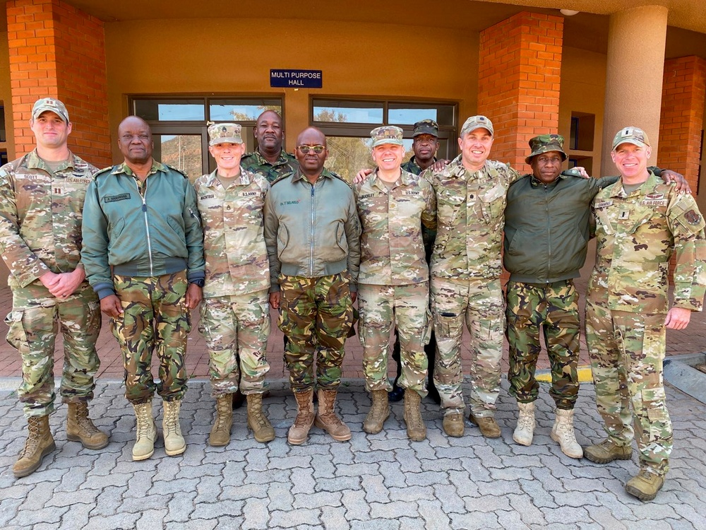 A group of approximately ten military personnel pose for a group photo in front of a building marked 'Multi Purpose Hall'. The group includes members wearing U.S. Army and U.S. Air Force uniforms in OCP/multicam pattern, alongside personnel in different camouflage uniforms consistent with an African military force. This appears to be a joint military engagement or partnership activity.