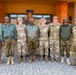 A group of approximately ten military personnel pose for a group photo in front of a building marked 'Multi Purpose Hall'. The group includes members wearing U.S. Army and U.S. Air Force uniforms in OCP/multicam pattern, alongside personnel in different camouflage uniforms consistent with an African military force. This appears to be a joint military engagement or partnership activity.