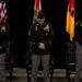 Three U.S. Army soldiers in dress green uniforms stand with heads bowed in what appears to be a formal military ceremony, likely a prayer or moment of reflection. They are positioned in front of multiple flags including the U.S. flag and what appears to be the Florida state flag and a unit flag. The setting appears to be an indoor ceremonial venue with ornate leather chairs visible behind them.