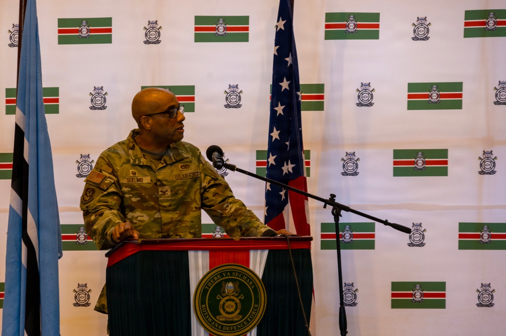 A U.S. Air Force officer is speaking at a podium bearing the Botswana Defence Force seal during what appears to be a bilateral military event. The backdrop features repeated Namibian flags and Botswana Defence Force insignia, while a U.S. flag and Botswana flag are visible on either side of the speaker. The name tape on the uniform reads 'SULLINS' and the uniform includes a U.S. flag patch.
