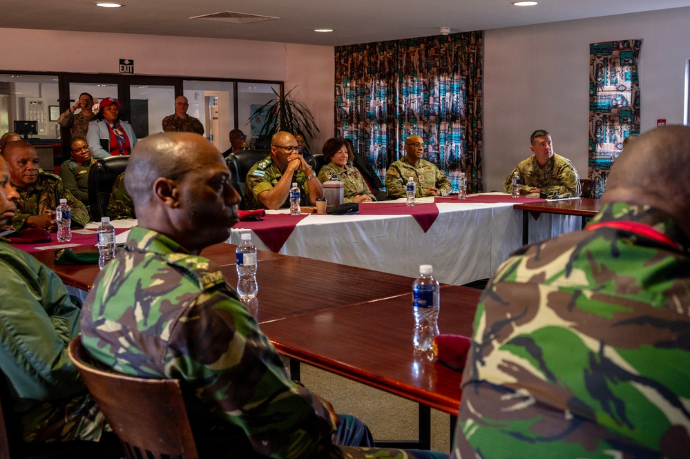 A multinational military meeting or briefing is taking place in a conference room. Personnel wearing multiple different camouflage uniforms — including US military MultiCam/OCP and green woodland-pattern camouflage worn by what appear to be African military personnel — are seated around tables arranged in a U-shape. The setting suggests a bilateral or multilateral military cooperation or liaison event.