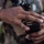 PANAMAX-26: V1/6, Partner forces conduct simulated air raid A close-up photograph showing the hands of a person wearing camouflage military uniform handling a black firearm magazine loaded with brass-cased rifle cartridges. The image focuses on the act of loading or inspecting ammunition. A firearm is partially visible in the blurred background.