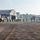 PANAMAX-26: V1/6, Partner forces conduct simulated air raid A line of military personnel in full combat gear is boarding or disembarking a CH-47 Chinook helicopter on a tarmac at what appears to be a military airfield. Large aircraft hangars are visible in the background along with urban buildings, suggesting a location near a city. The scene depicts a tactical troop movement or training exercise.
