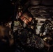 Military personnel are seated inside what appears to be a military transport aircraft or helicopter, packed closely together in full combat gear. The image is taken from inside the aircraft looking toward the rear opening, with dramatic side lighting illuminating the closest soldier. The soldiers are wearing camouflage uniforms and tactical equipment, suggesting an active deployment or training operation.