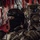 PANAMAX-26: V1/6, Partner forces conduct simulated air raid Three military personnel are seated inside what appears to be a military helicopter or transport aircraft, identifiable by the red interior framing and cargo netting. The soldiers are wearing varied tactical gear including helmets, body armor, and communication equipment. At least two different national forces appear to be represented based on visible patches and equipment differences.