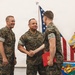 Three U.S. Marines in MARPAT woodland camouflage uniforms are participating in a formal military ceremony at MCAS Miramar. The central figure, whose name tape reads 'GARCIA,' is shaking hands with a younger Marine who is holding a red award folder bearing the Marine Corps emblem. A third Marine, whose name tape appears to read 'MAYFIELD,' stands to the left smiling broadly.