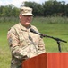 A U.S. Army officer with the name tape 'ROGERS' is speaking at a wooden podium with a microphone in an outdoor setting. The officer wears the Army Combat Uniform (OCP/MultiCam) and displays two stars on the chest, indicating the rank of Major General. The setting appears to be a formal military ceremony or event held on a grassy field.