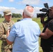 A U.S. Army officer wearing camouflage uniform with the name tape 'ROGERS' and two-star general rank insignia is being interviewed by a television news crew outdoors. A reporter holding a microphone faces the general while a cameraman operates a professional video camera. The setting appears to be an open field or training area on a sunny day.