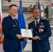 Two U.S. Air Force officers are posing together holding a certificate from the State of Florida titled 'The Florida Cross' for Extraordinary Meritorious Service. The ceremony appears to be taking place inside a military hangar, with the Florida state flag and blue Air Force flags visible in the background. The officer on the right is wearing multiple medals and decorations, suggesting this is a formal military awards ceremony.