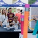 A family-friendly outdoor event organized by MWR (Morale, Welfare, and Recreation) at CFА Yokosuka, a U.S. Navy installation in Japan. Participants are gathered around a game booth featuring a ring-toss activity using oversized pencil-shaped posts. Children and adults are engaging with the activity booth while staff assist.
