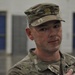 A young male U.S. Army soldier is shown in close-up, wearing Operational Camouflage Pattern (OCP) uniform and patrol cap with a unit crest insignia. He appears to be indoors in a military facility, possibly speaking or being interviewed. The background shows blue-doored lockers or storage units in a blurred gymnasium or armory-type space.