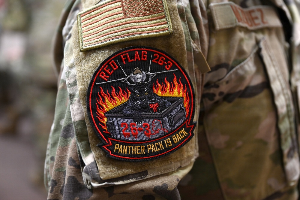 The image shows a close-up of a military uniform sleeve displaying two patches. The upper patch is a subdued American flag, and below it is a circular morale patch for 'Red Flag 26-3' with the motto 'Panther Pack Is Back.' A partial name tape reading 'VALDEZ' (or similar) is visible on the adjacent uniform.