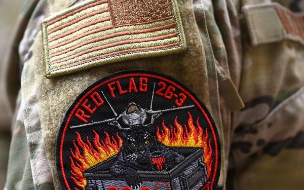 The image shows a close-up of a military uniform sleeve displaying two patches. The upper patch is a subdued American flag, and below it is a circular morale patch for 'Red Flag 26-3' with the motto 'Panther Pack Is Back.' A partial name tape reading 'VALDEZ' (or similar) is visible on the adjacent uniform.