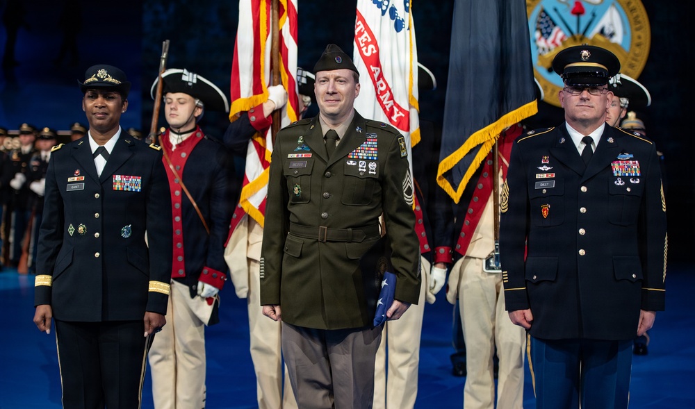 A formal U.S. Army military ceremony featuring three prominent figures standing at the forefront, with a color guard in historical Continental Army uniforms behind them. The central figure, wearing an olive green Army Service Uniform with a garrison cap, holds a folded American flag, suggesting a retirement or change-of-responsibility ceremony. The event appears to be held in a large indoor venue with Army insignia displayed in the background.
