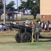 Two U.S. Army soldiers in camouflage uniforms stand beside a ceremonial artillery cannon on a military installation. The cannon bears inscriptions reading 'U.S. ARMY', '2LT CHILDERS MH 1943', and 'BROKEN ARROW, OK'. A large group of people, many in civilian clothing, are gathered in the background, suggesting a military ceremony or demonstration event.