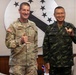Two military officers are posing together for a formal photo, both making 'shaka' or thumbs-up hand gestures and smiling. The officer on the left wears a U.S. Army OCP (Operational Camouflage Pattern) uniform with the name tape 'VOWELL' and four-star rank insignia, along with a U.S. flag patch. The officer on the right wears a Thai military digital camouflage uniform with a Thai flag patch, suggesting this is a bilateral military meeting.
