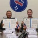 Two military officers, one from the Royal Thai Army and one from the U.S. Army, are seated at a conference table holding up signed documents in blue folders. Name placards identify them as LTG Pongsak Munklahan (Deputy Chief of Staff Operations, Royal Thai Army) and LTG JB Vowell. The setting appears to be a formal bilateral military agreement signing ceremony, with Thai and American flags visible on the table and a military unit insignia (red arrow with stars) displayed on the wall behind them.