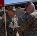 A U.S. Marine Corps ceremony is taking place outdoors, where a senior Marine is pinning a medal or award onto the uniform of a Marine identified by the name tape 'Rodriguez.' A red guidon flag marked 'CLB-5' (Combat Logistics Battalion 5) is visible in the foreground, and a formation of Marines stands in the background.