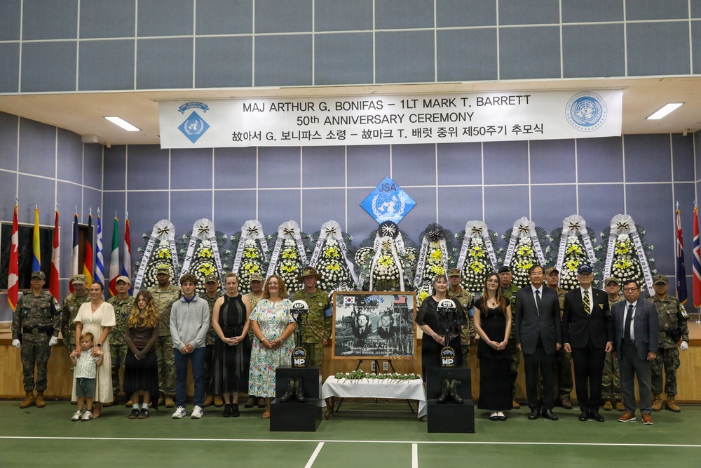 This image depicts the 50th Anniversary Ceremony honoring Major Arthur G. Bonifas and 1st Lieutenant Mark T. Barrett, two U.S. Army officers killed in the 1976 Korean DMZ axe murder incident. The ceremony is held at the Joint Security Area (JSA) and features military personnel, civilian attendees (likely family members), floral wreaths, and memorial displays. A banner in both English and Korean identifies the occasion, and multiple national flags are visible in the background.