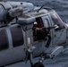 A U.S. Navy military helicopter, marked with 'CVW-9 LINCOLN' and tail code 'CIF', is flying over open water. A crew member wearing a flight helmet and visor is visible manning a door-mounted machine gun from the open side door. The word 'RESCUE' is stenciled on the fuselage, identifying this as likely an MH-60S or MH-60R Seahawk helicopter.