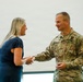 A U.S. Army officer identified by name tape as 'CARPENTER' is shaking hands with a civilian woman during what appears to be a formal recognition or award ceremony. The soldier, wearing an OCP (Operational Camouflage Pattern) uniform with a Brigadier General star insignia, is holding what appears to be a glass award or plaque. Both individuals are smiling, suggesting a positive and celebratory interaction.