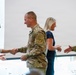 A formal greeting scene showing two military personnel in camouflage uniforms shaking hands with two civilian women in what appears to be an official or ceremonial setting. The interaction appears cordial and professional, with all four individuals smiling. The setting appears to be an indoor facility with large windows in the background.